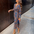 Woman wearing a long-sleeved wrap maxi dress with a bold print pattern, styled with gold heels and jewelry for a wedding guest look._0