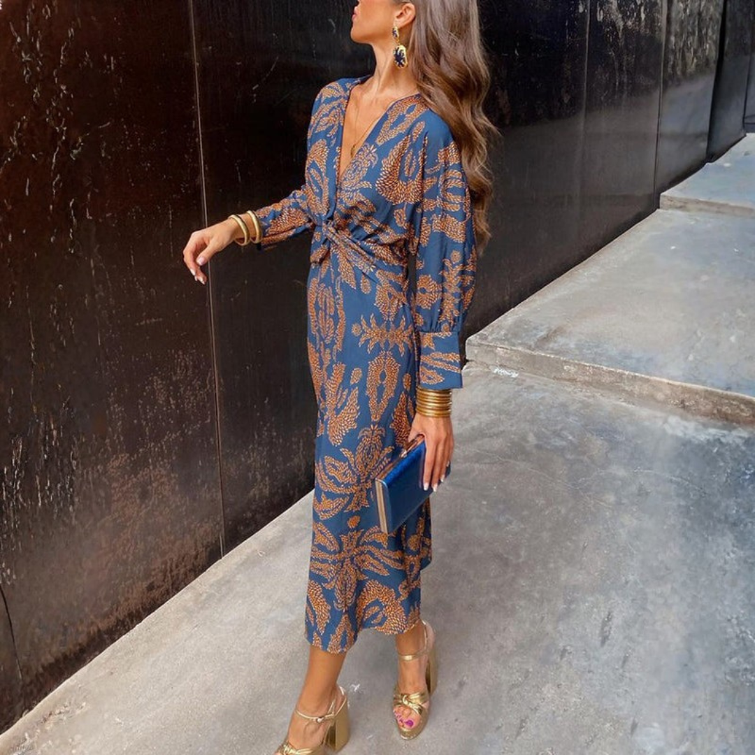 Woman wearing a long-sleeved wrap maxi dress with a bold print pattern, styled with gold heels and jewelry for a wedding guest look._0