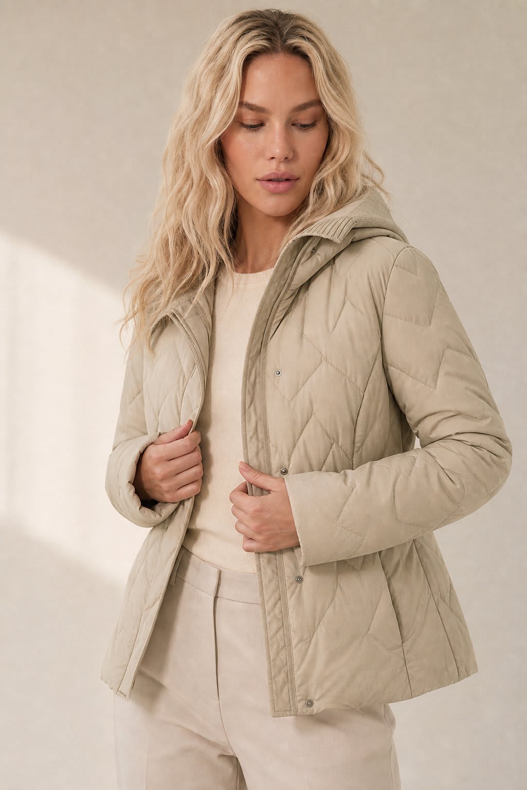 Woman wearing a quilted hooded jacket in a neutral tone with knit hood detail._0