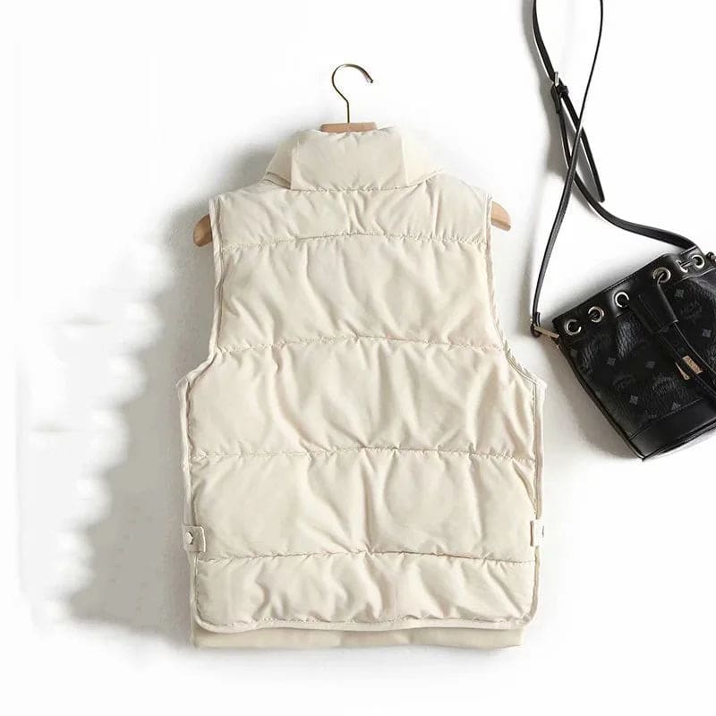 Model wearing a cream quilted vest with stand collar over a neutral sweater and brown trousers._11