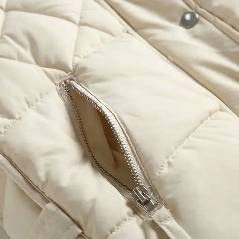Model wearing a cream quilted vest with stand collar over a neutral sweater and brown trousers._14