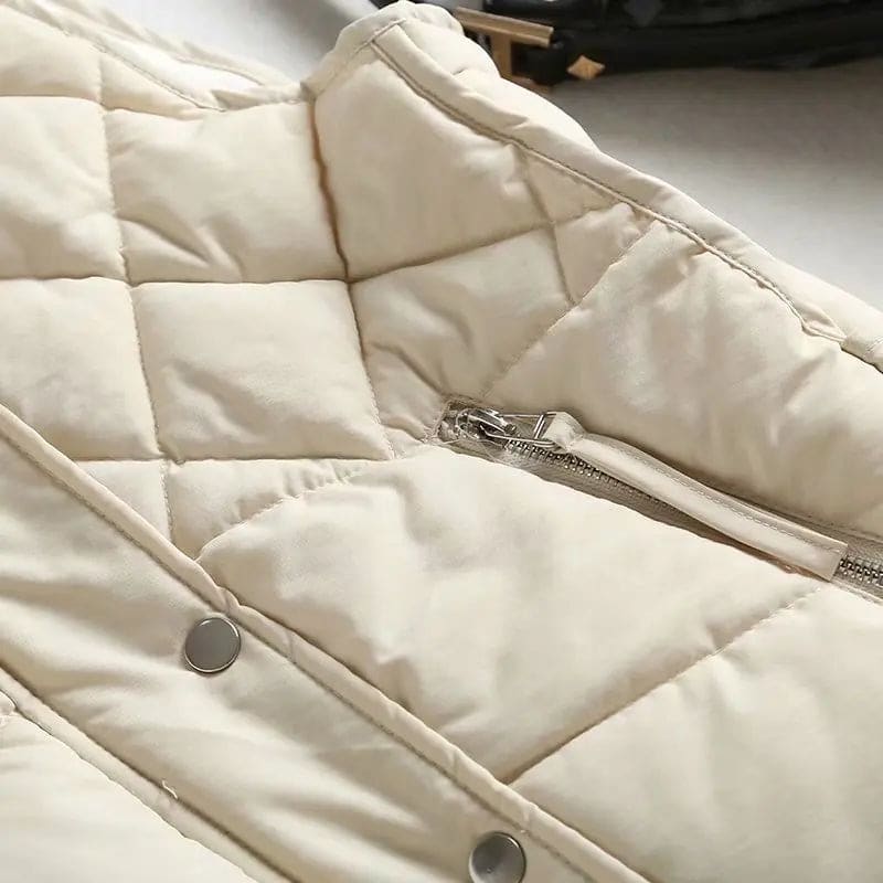 Model wearing a cream quilted vest with stand collar over a neutral sweater and brown trousers._15