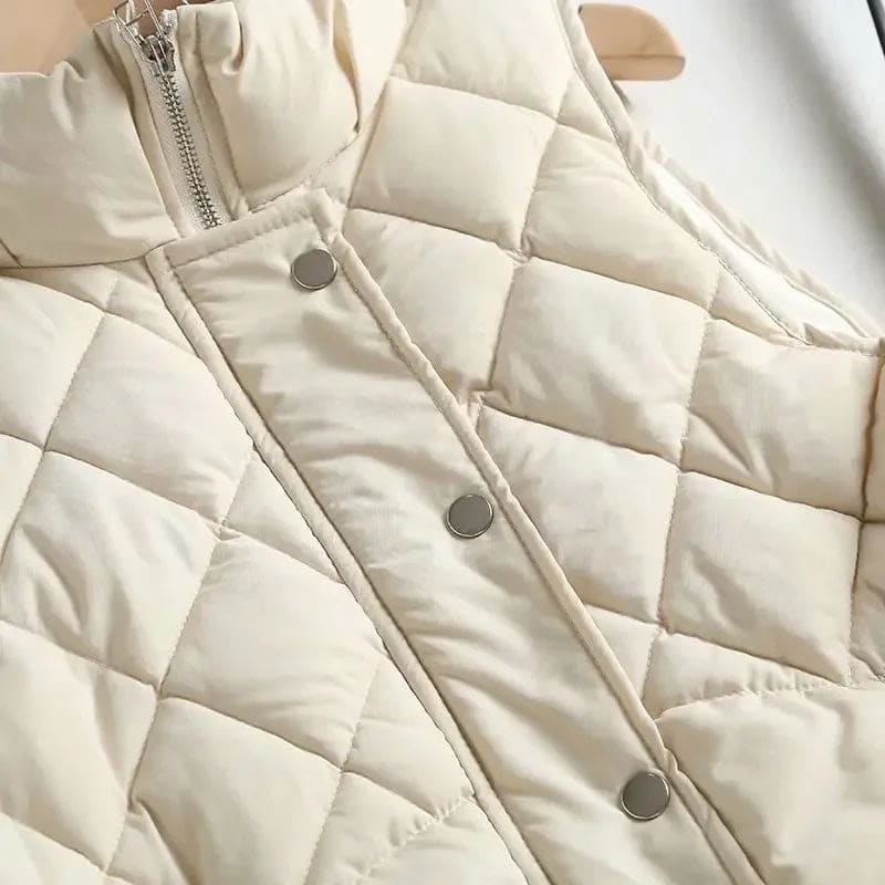 Model wearing a cream quilted vest with stand collar over a neutral sweater and brown trousers._21