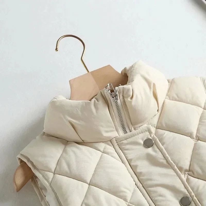 Model wearing a cream quilted vest with stand collar over a neutral sweater and brown trousers._7
