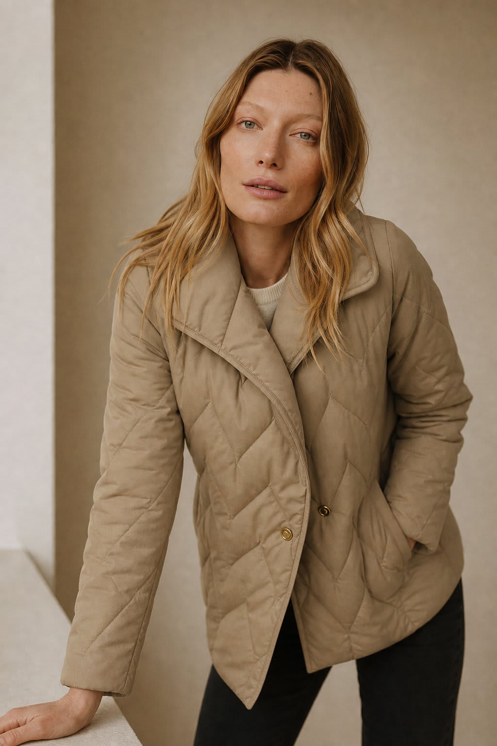 Woman wearing a quilted jacket with wrap front and tie belt in a warm neutral tone._4