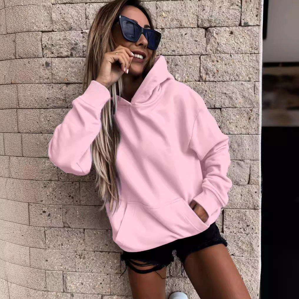 Relaxed pink pullover hoodie with a roomy hood, long sleeves, and front pocket, styled with black shorts.