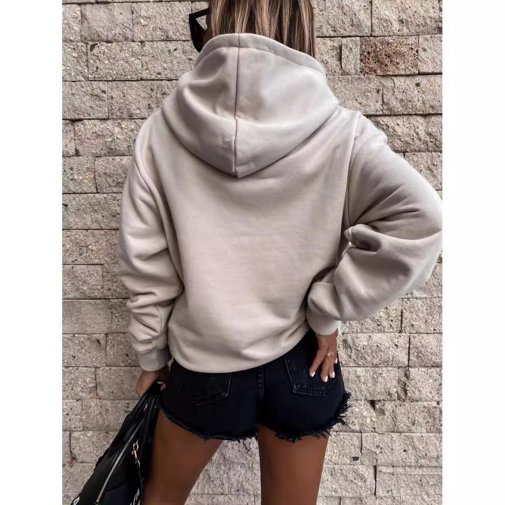 Back view of a light neutral pullover hoodie showing the hood, relaxed shoulders, long sleeves, and ribbed hem.