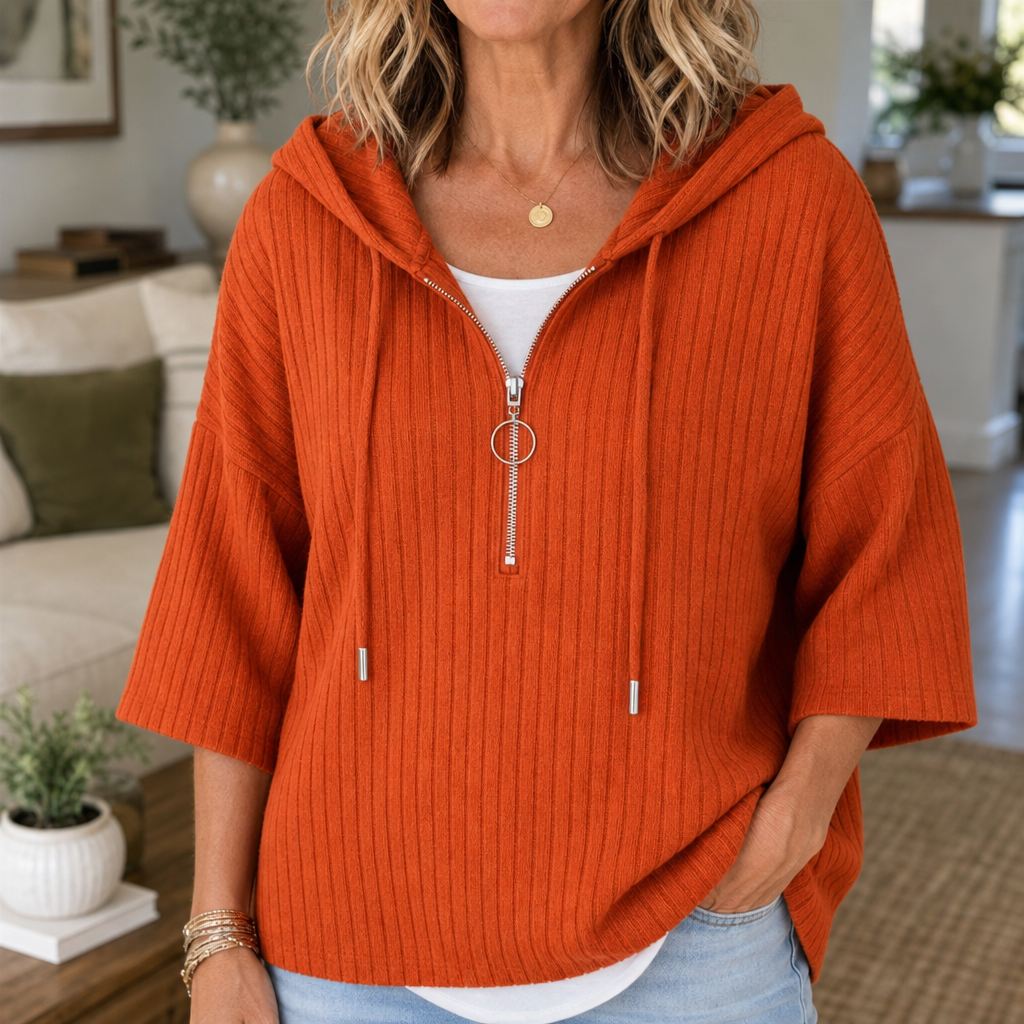 Close front view of an orange ribbed hooded top with a half-zip neckline, ring zipper pull, drawstrings, and elbow-length sleeves.