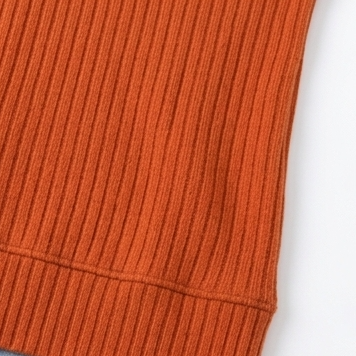 Detail view of the orange ribbed top’s lower hem and side seam.