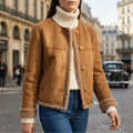 Woman wearing a collarless jacket with shearling trim and gold buttons, paired with a cream turtleneck and jeans on a city street._0