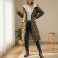 Woman wearing a long olive green puffer coat with sherpa lining and hood, styled with jeans and brown boots indoors._0