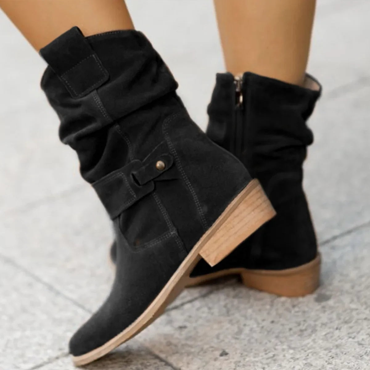 Black slouchy mid-calf boot shown in profile with a pointed toe, ankle buckle, side zipper, and contrasting low heel.