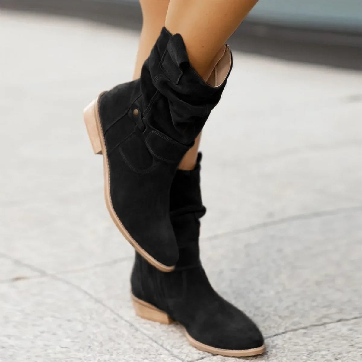Black boots modeled in a crossed-leg pose, emphasizing the relaxed gathered shaft, pointed toe, and flat sole.