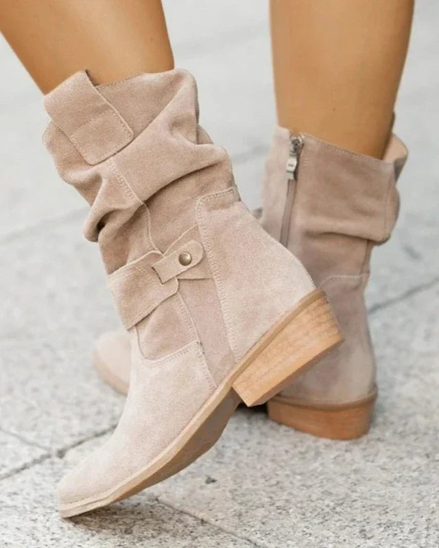 Light beige slouchy boots shown from the side with gathered shafts, buckle details, side zipper, and low block heels.