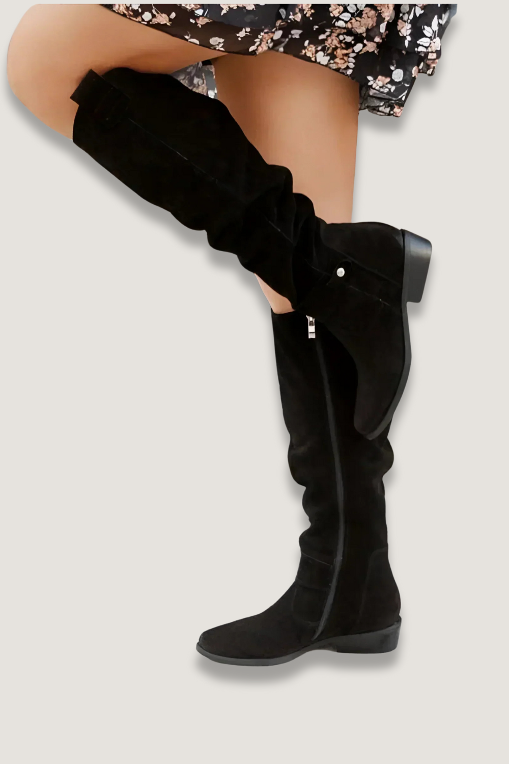 Black slouchy knee-high boot with a low block heel shown in profile beneath a floral skirt.