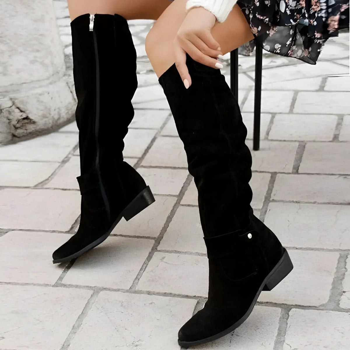 Pair of black slouchy knee-high boots shown from the back and side, featuring visible zippers and low heels.