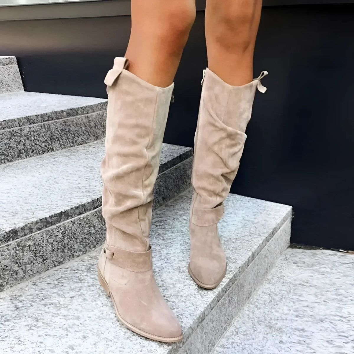 Pair of beige knee-high boots displayed from the front, highlighting their gathered shafts, pointed toes, and low heels.