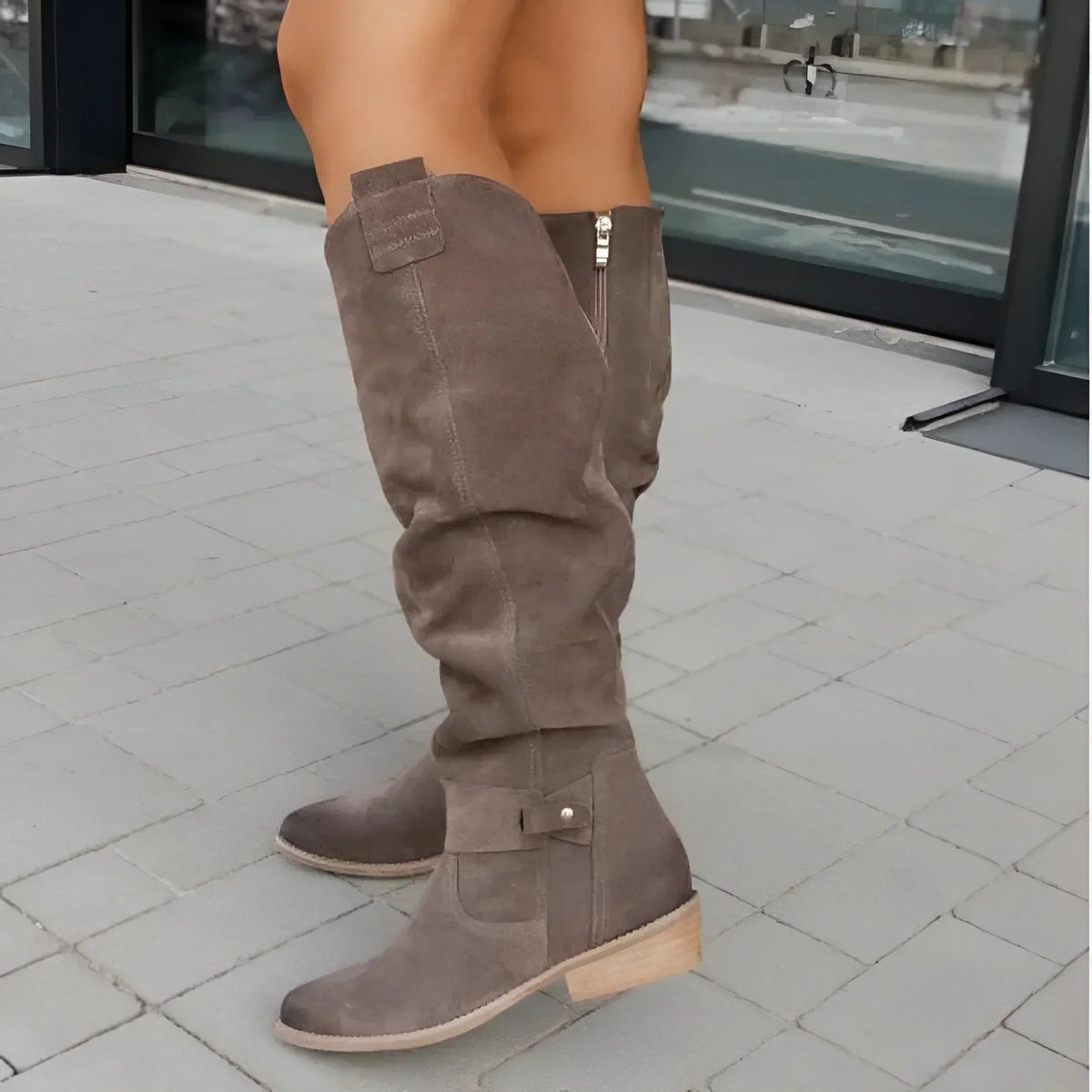 Taupe knee-high boot shown from the outer side with layered strap details, a side zipper, and a low wooden-look heel.