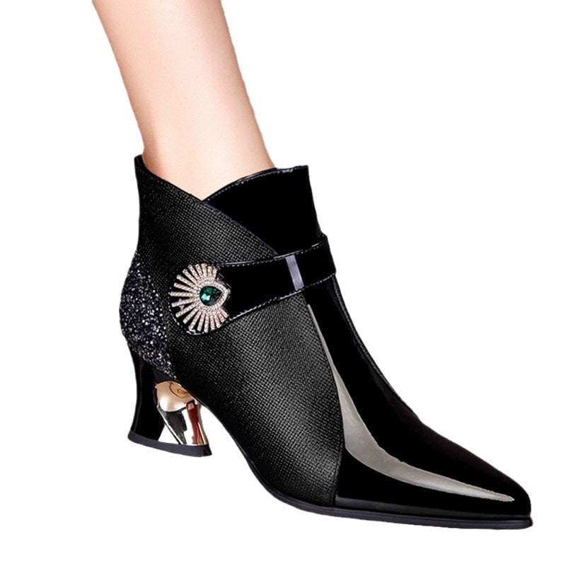 Single black ankle boot in profile with a glossy pointed toe, jeweled strap detail, sparkling heel panel, and reflective sculpted heel.