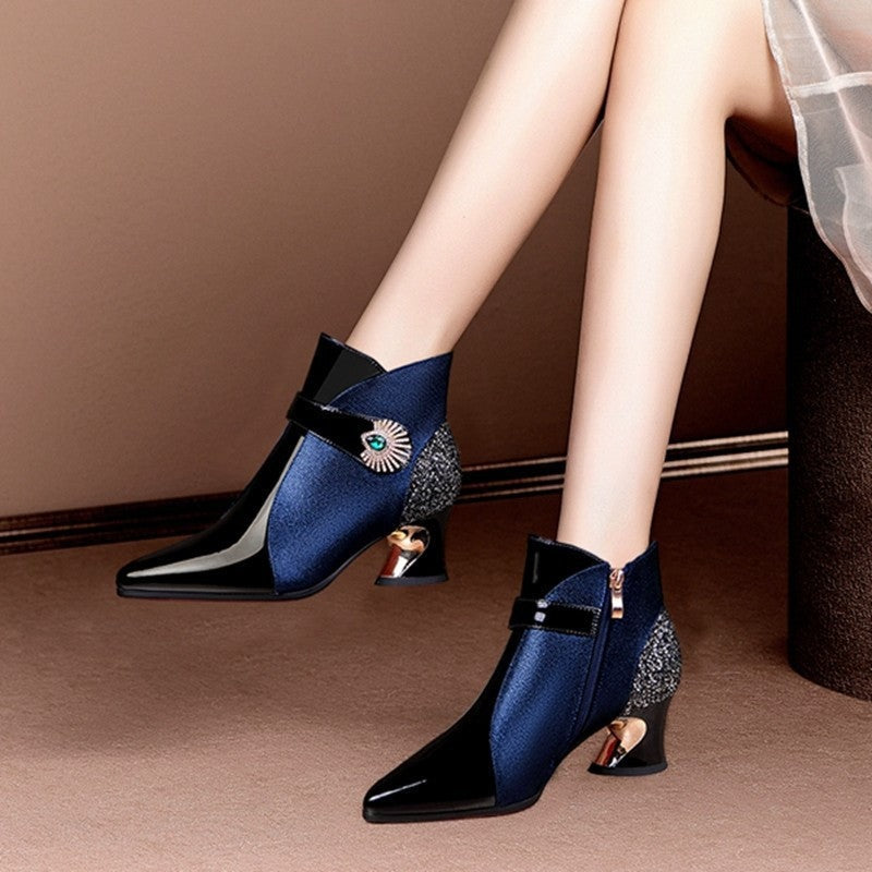 Navy and black ankle boots posed beside a seat, with one boot showing its side zipper and both displaying glittering panels and sculpted heels.