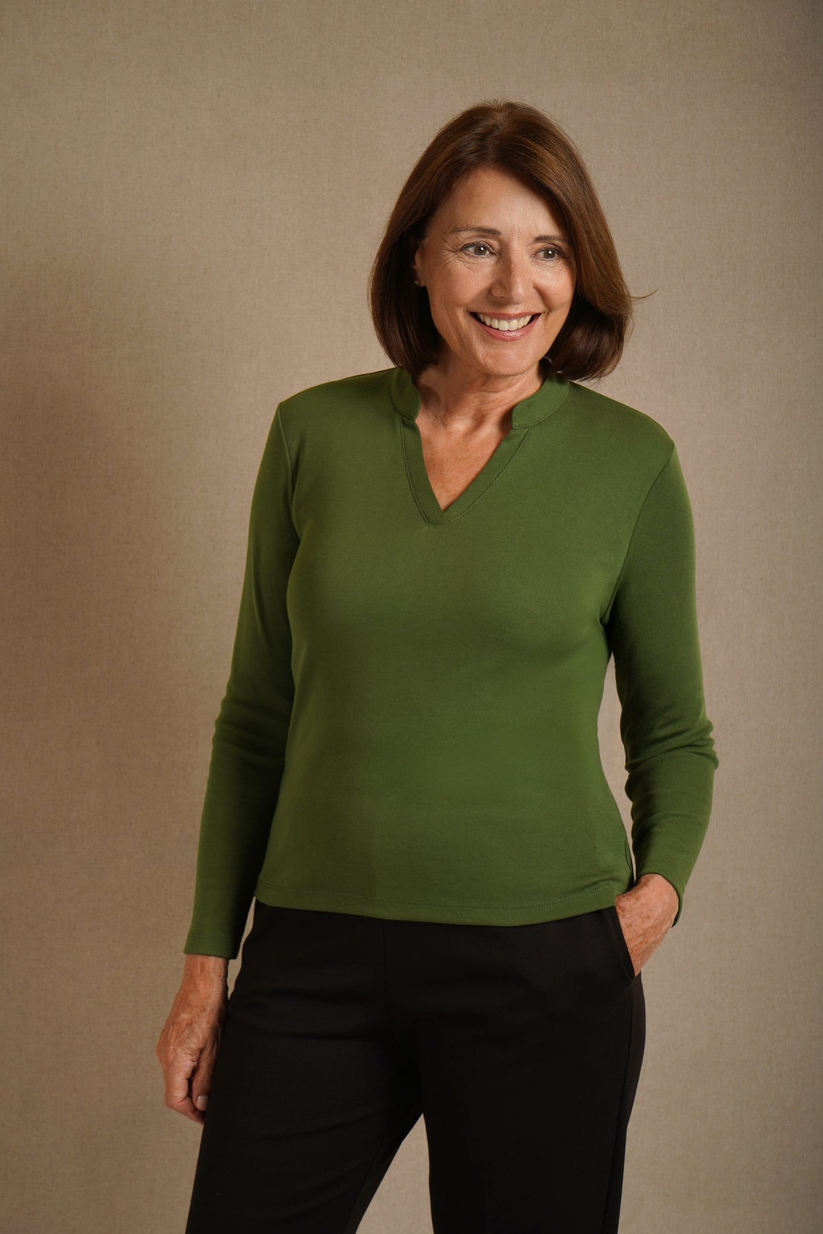 Woman wearing an olive green long sleeve top with a split stand-up neckline and black trousers._0
