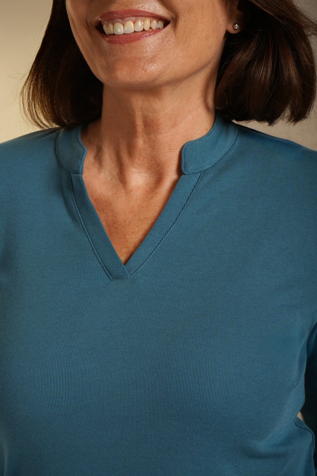Woman wearing an olive green long sleeve top with a split stand-up neckline and black trousers._3