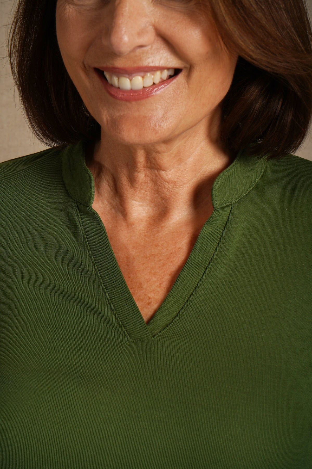 Woman wearing an olive green long sleeve top with a split stand-up neckline and black trousers._4
