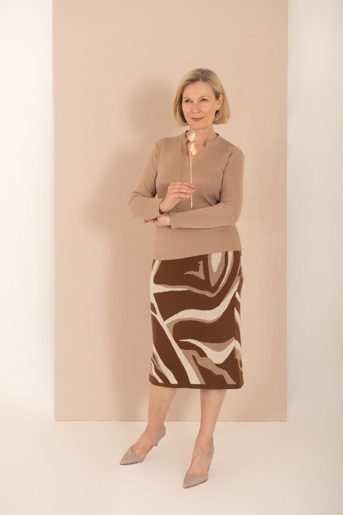 Woman wearing an olive green long sleeve top with a split stand-up neckline and black trousers._7