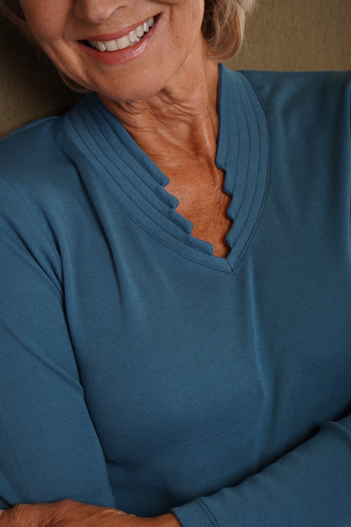 Smiling woman wearing a blue long sleeve top with a ribbed stand-up collar and scalloped V-neckline, paired with a grey skirt._1