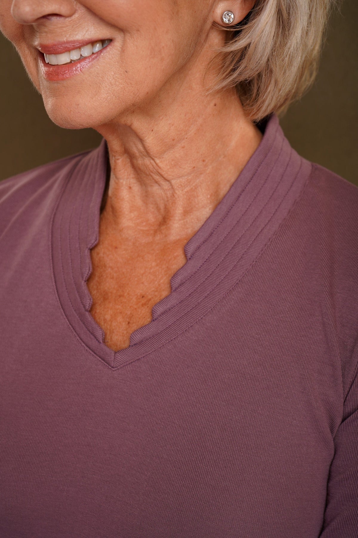 Smiling woman wearing a blue long sleeve top with a ribbed stand-up collar and scalloped V-neckline, paired with a grey skirt._3