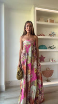 Woman wearing a strapless floral maxi dress with empire waist and colorful print, standing indoors with shelves in the background._0