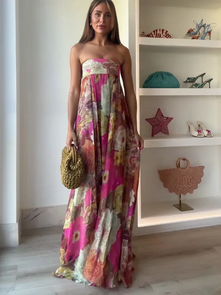 Woman wearing a strapless floral maxi dress with empire waist and colorful print, standing indoors with shelves in the background._1