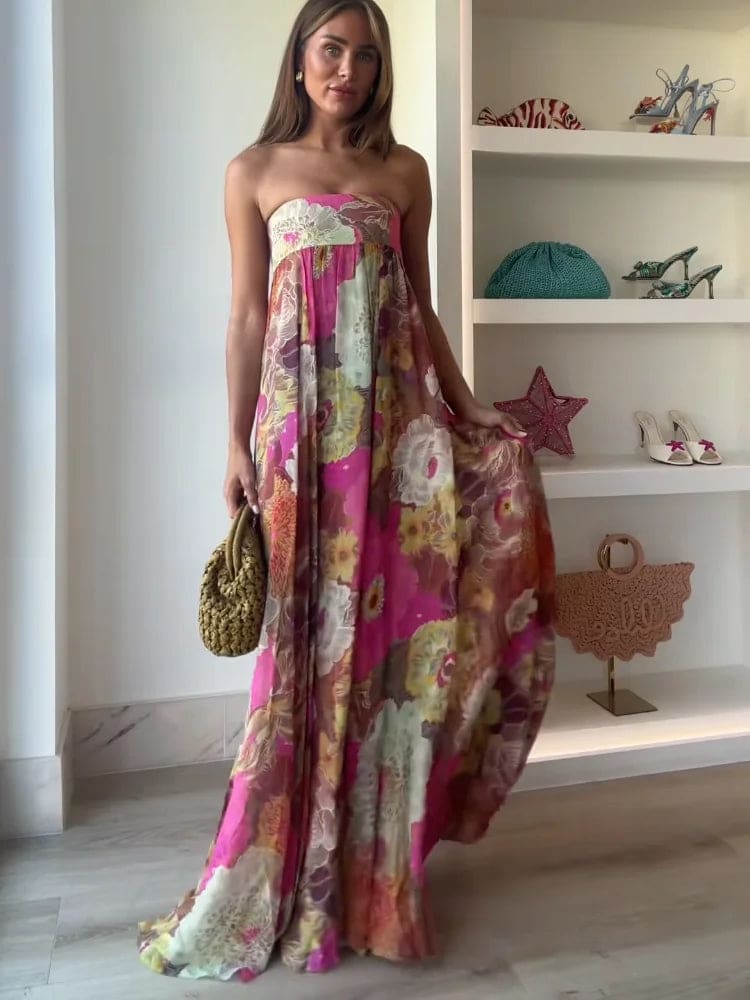 Woman wearing a strapless floral maxi dress with empire waist and colorful print, standing indoors with shelves in the background._2