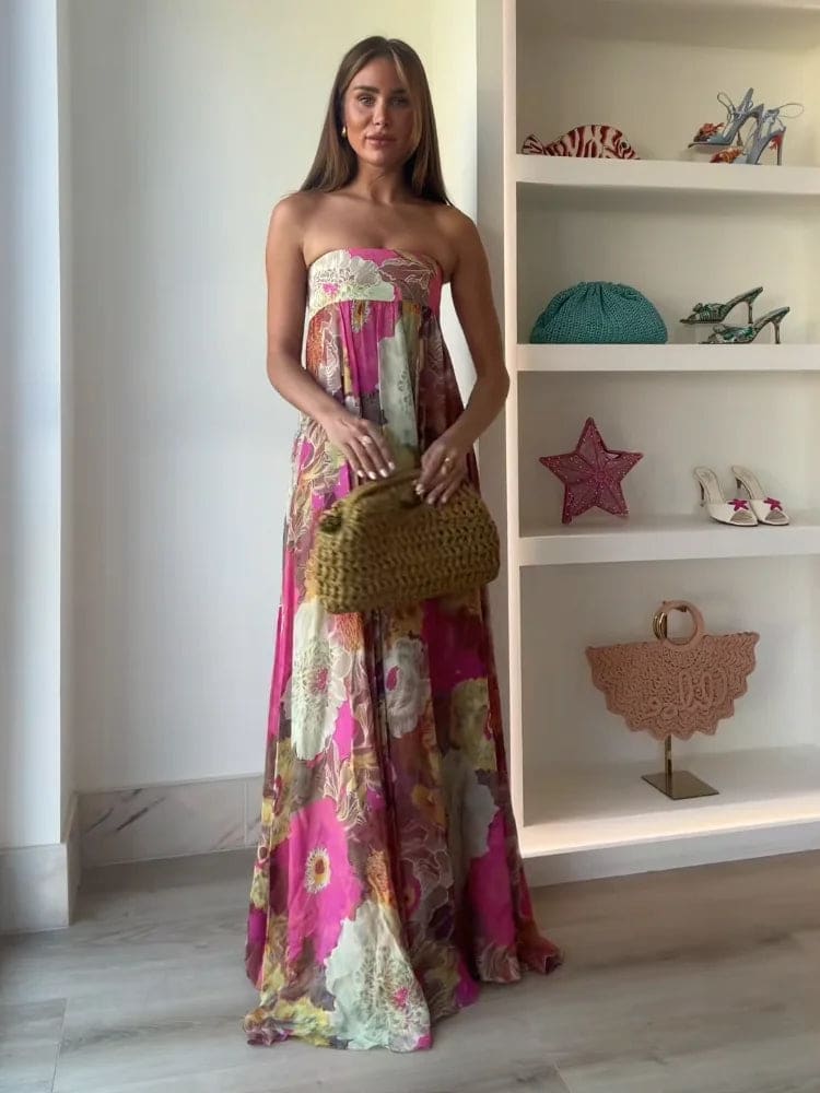 Woman wearing a strapless floral maxi dress with empire waist and colorful print, standing indoors with shelves in the background._3