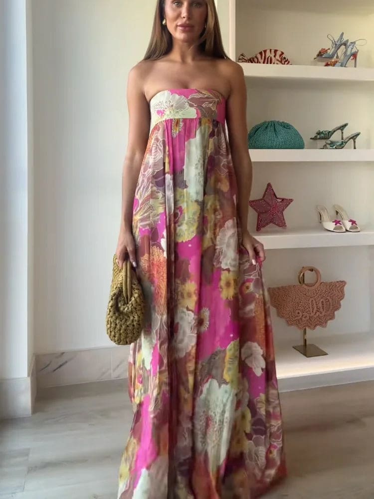 Woman wearing a strapless floral maxi dress with empire waist and colorful print, standing indoors with shelves in the background._4