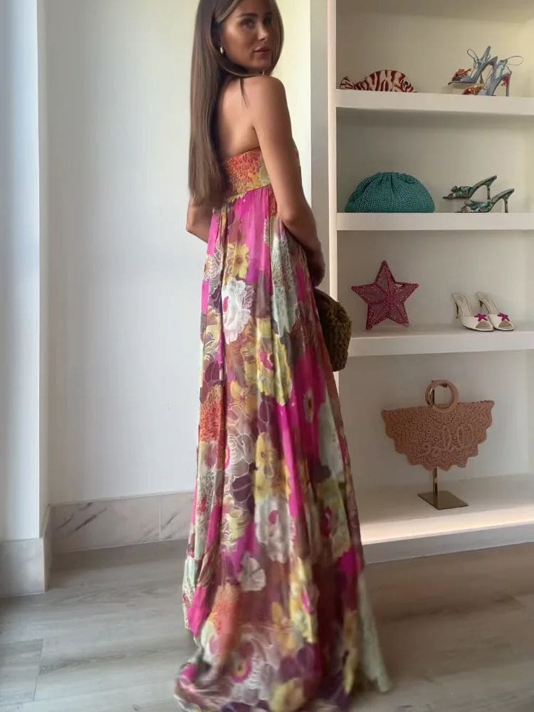 Woman wearing a strapless floral maxi dress with empire waist and colorful print, standing indoors with shelves in the background._5