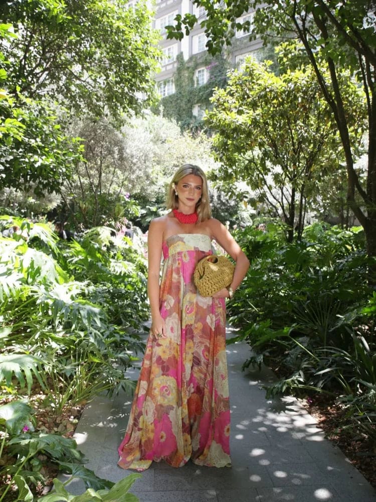 Woman wearing a strapless floral maxi dress with empire waist and colorful print, standing indoors with shelves in the background._6