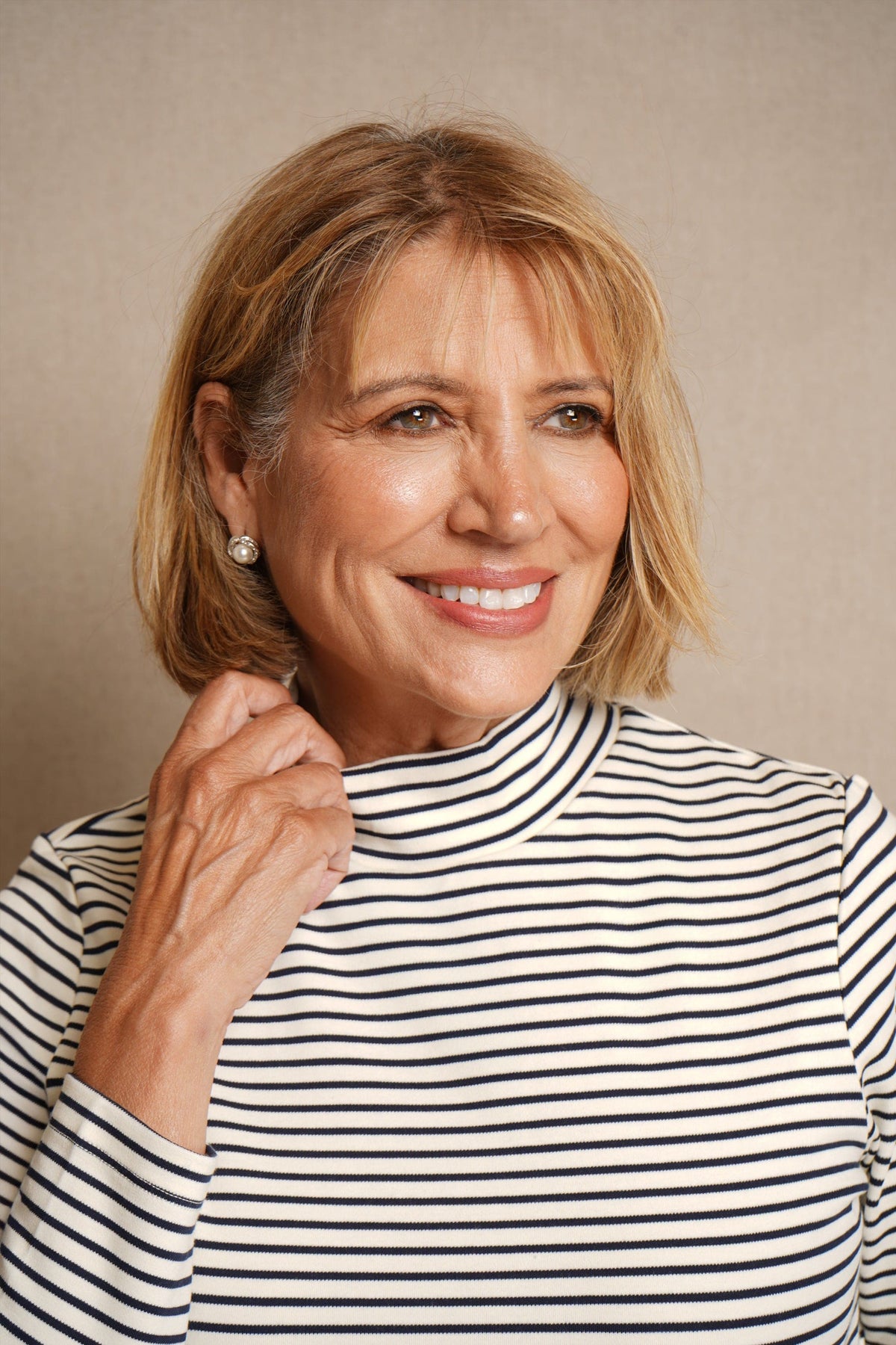 Woman wearing a cream and navy striped long sleeve mock neck top with dark blue jeans against a beige background._1