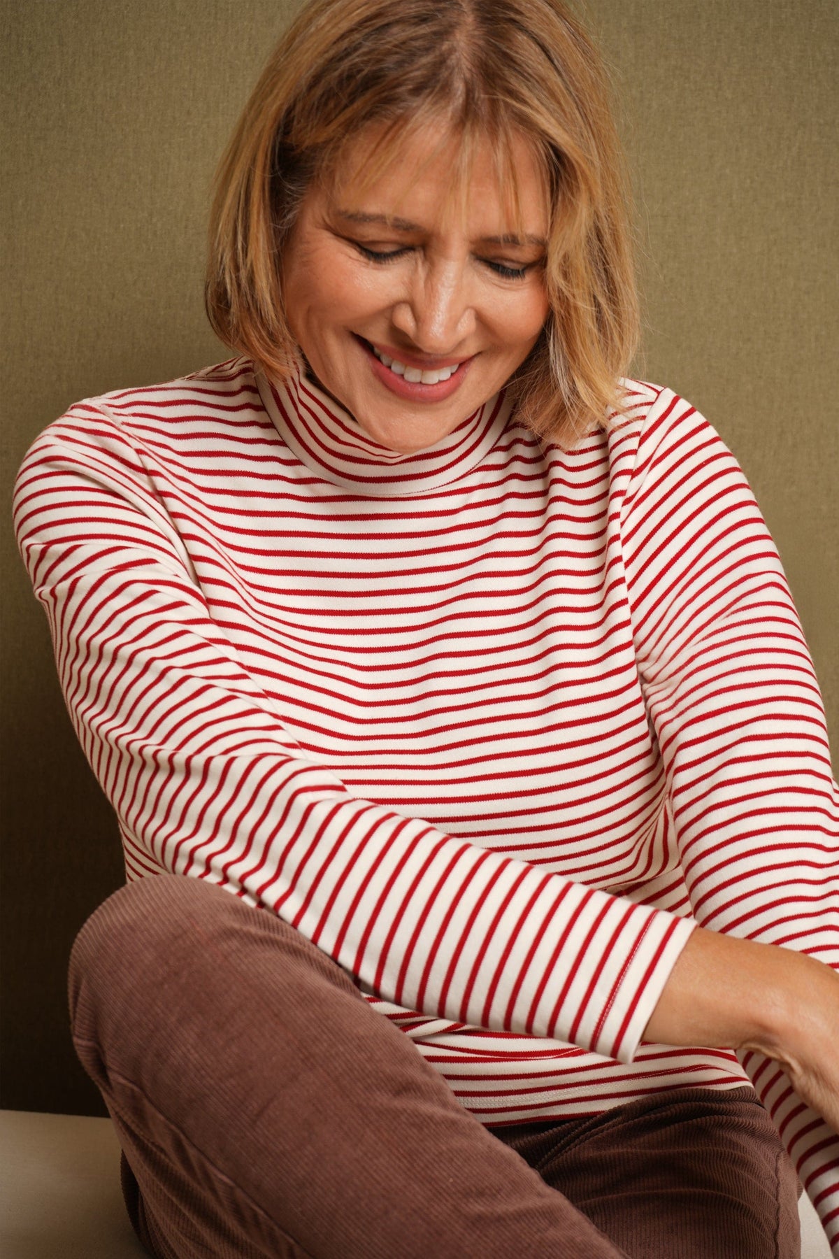 Woman wearing a cream and navy striped long sleeve mock neck top with dark blue jeans against a beige background._4