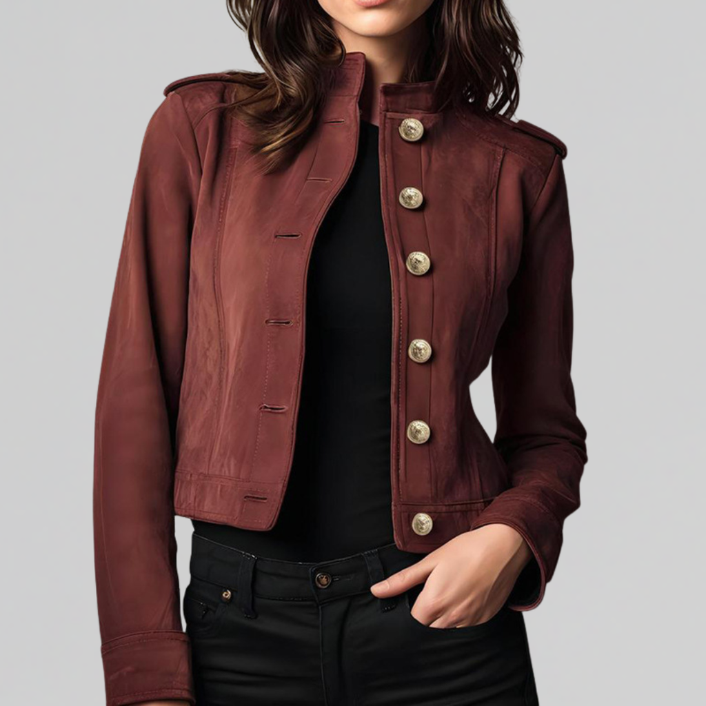 Woman wearing a cropped military-style jacket with gold button detail and stand collar, styled over a black top and pants._0