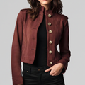 Woman wearing a cropped military-style jacket with gold button detail and stand collar, styled over a black top and pants._0