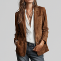 Woman wearing a structured brown blazer layered over a white button-down blouse with jeans and layered necklaces._0