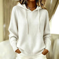 Woman wearing a white long sleeve hooded knit pullover with a drawstring hood, ribbed cuffs and ribbed hem, with white trousers and layered gold necklaces._0