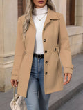Woman wearing a tailored trench coat with notched lapel, double breasted button front, and tab details, styled over a white turtleneck and jeans._0