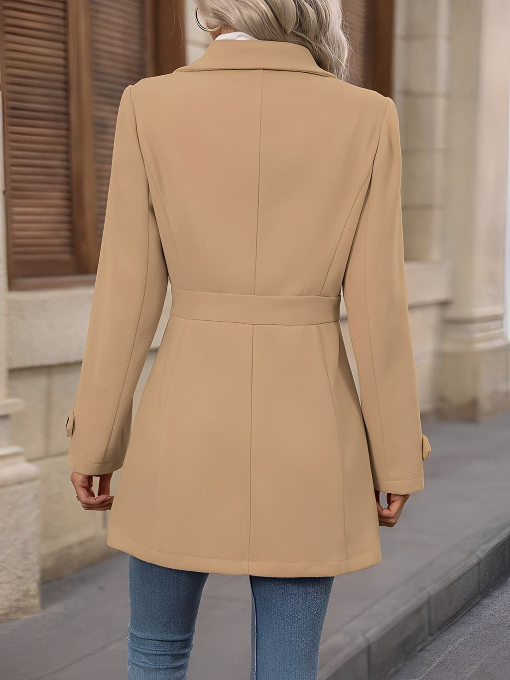 Woman wearing a tailored trench coat with notched lapel, double breasted button front, and tab details, styled over a white turtleneck and jeans._1