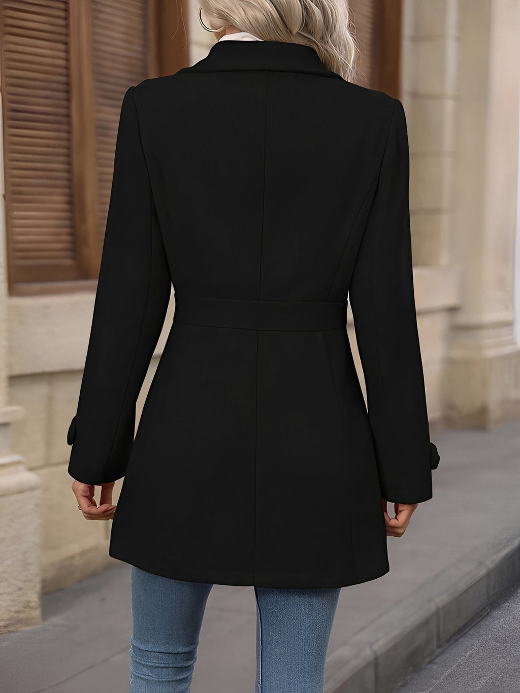 Woman wearing a tailored trench coat with notched lapel, double breasted button front, and tab details, styled over a white turtleneck and jeans._17