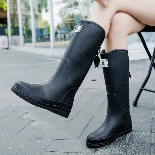 Woman wearing tall waterproof boots with adjustable back strap while seated outdoors._0