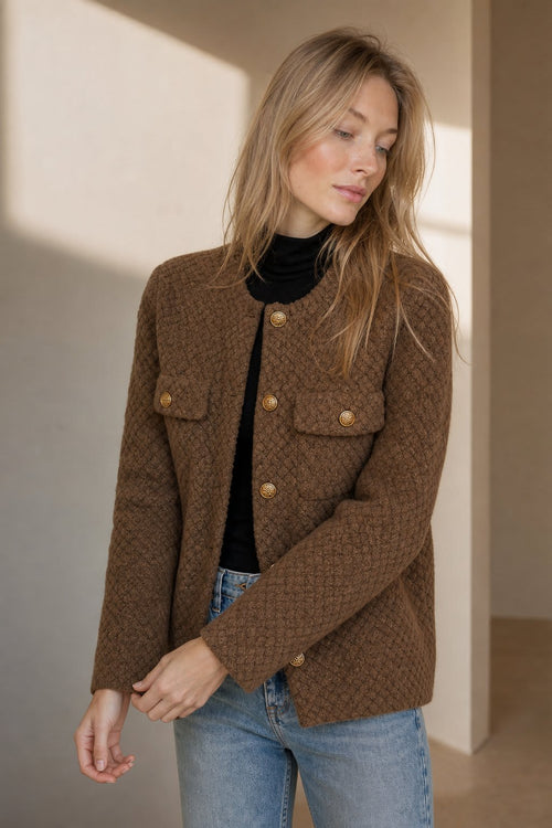 Woman wearing a textured short jacket with gold buttons in a tailored silhouette, viewed from behind._2
