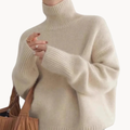 Woman wearing a cream oversized turtleneck sweater with ribbed detailing and relaxed fit, styled with a tan handbag._0