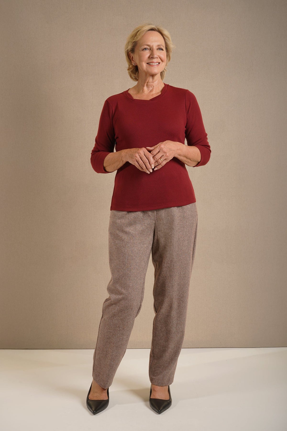Woman wearing a navy three quarter sleeve scoop neck top with contrast neckline trim, grey trousers and black pointed heels._1
